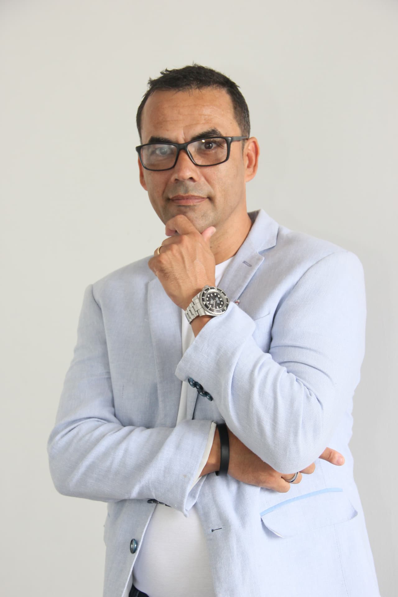 Retrato de Guto Azevedo, de blazer claro e óculos, com os braços cruzados.